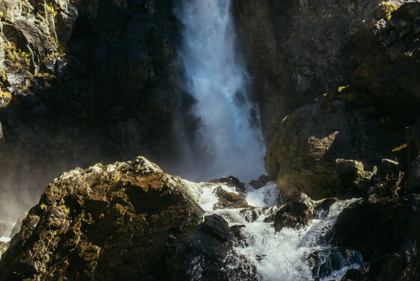 istock Atmospheric minimal landscape with vertical big waterfall on rock mountain wall. Powerful large waterfall in dark gorge. Nature background of high vertical turbulent falling water stream on wet rocks. 1335130892