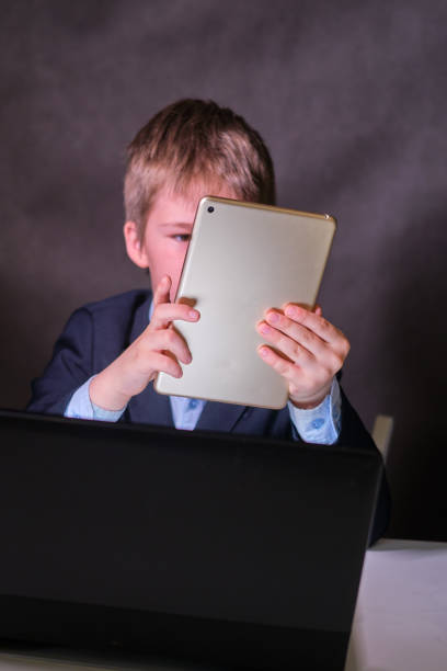 istock A happy boy in a school suit with a digital tablet in his hands, copy space on a dark studio background 1335130937
