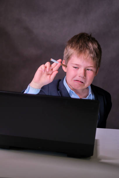 istock A boy in a school suit with a cigarette at the computer, copy space on a dark studio background 1335130939