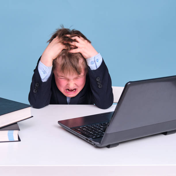 un niño asustado en un traje de la escuela en la educación a distancia, espacio de copia en un fondo de estudio azul - furious blue little boys caucasian fotografías e imágenes de stock