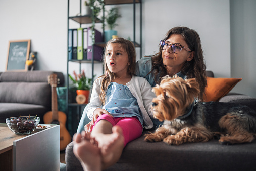 Beautiful family sitting on the couch and watching TV with their lovely dog