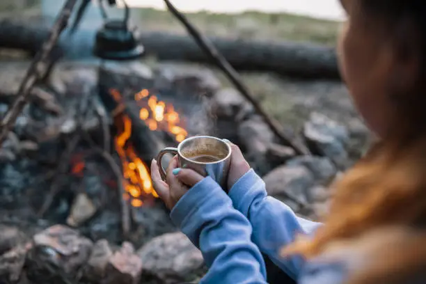 Photo of Woman holding hot drink next to campfire