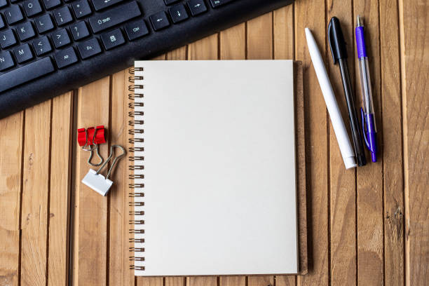 leer geöffnetes abgeschnittenes tagebuch neben einer tastatur stifte auf dem holzschreibtisch. leer öffnen sie den notizblock mit clip und bleistiften in der nähe der tastatur auf dem tisch platziert. - spiral notebook stock-fotos und bilder