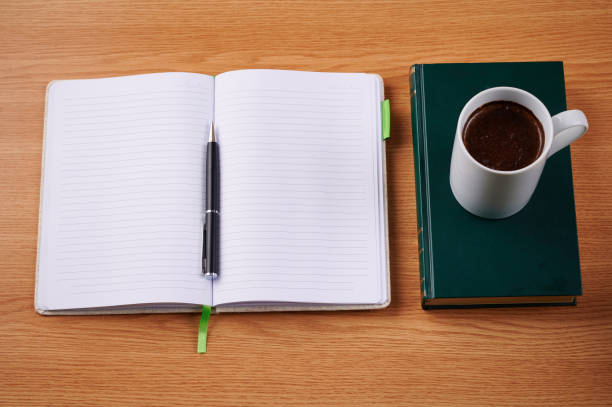 istock Plain Blank Notebooks And A Pen Beside A Cup Of Coffee Placed Book Table. Simple Empty Notepads With A Ballpen And Mug Over Dictionary Desk. 1335131690