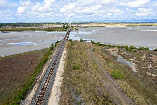 Drone flight along a rail line and towards a bridge crossing over a tidal coastal creek. St Lawrence, Queensland, Australia
