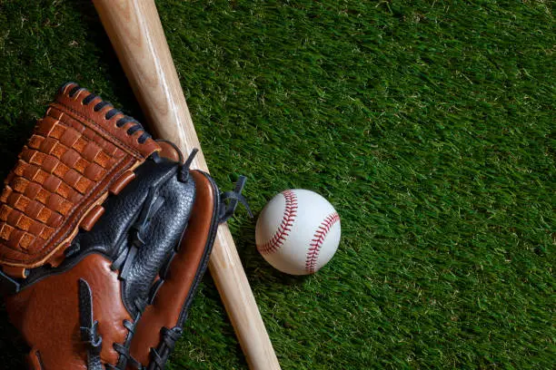 Baseball and wood bat with mitt on grass field overhead view