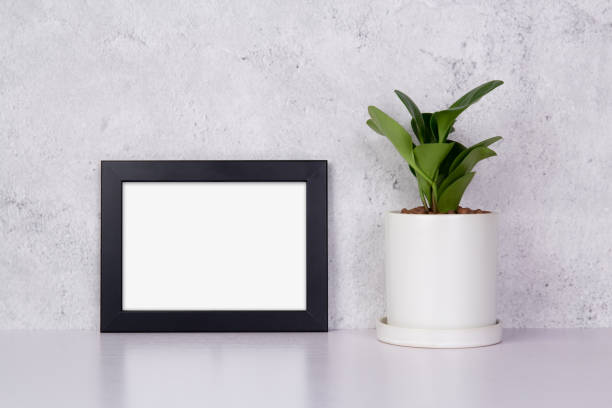 istock Mockup black frame horizontal and plants in pot on table top at home, mock up poster for presentation, your design for gallery photo and picture, border template and decoration for advertising. 1335149027