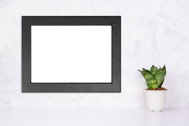 istock Mockup black frame horizontal on the wall and plants in pot on table top at home, mock up poster for presentation on desk, your design for gallery photo and picture, border template for advertising. 1335149034