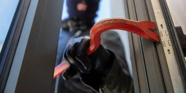 Photo of Bandit in balaclava holding a crowbar to break a glass window.