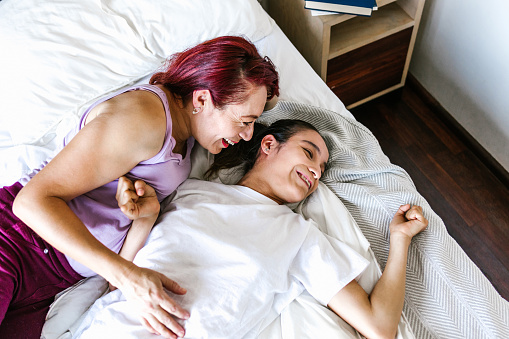 Hispanic teen girl with cerebral palsy lying in bed with her mother smiling, in disability concept in Latin America