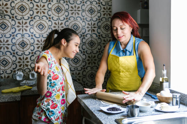 ragazza ispanica con paralisi cerebrale e sua madre che cucina a casa, nel concetto di disabilità in america latina - brain case foto e immagini stock