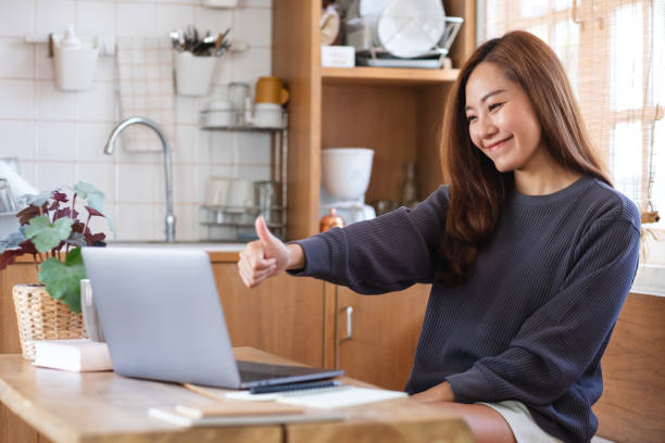 istock A young asian woman making thumbs up hand sign while using laptop computer for video call and working online at home 1335167846