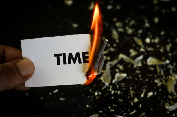 istock burning time, human hand holding the word time written on a paper burning with flame and ashes on a black background, concept 1335172049