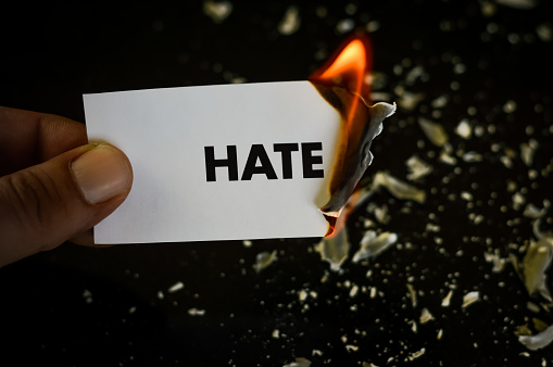 burning hate, human hand holding the word hate written on a paper burning with flame and ashes on a black background, concept