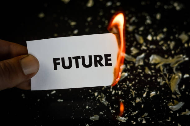 istock burning future, human hand holding the word future written on a paper burning with flame and ashes on a black background, concept 1335172090