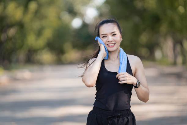 A healthy happy Asian woman runner in black sport outfits jogging in the natural city park under evening sunset stock photo