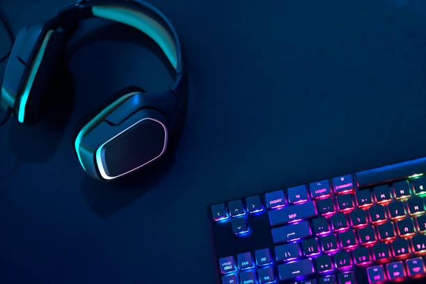 istock Headphones laying on desk next to rainbow colors backlighted gaming computer keyboard. 1335174032