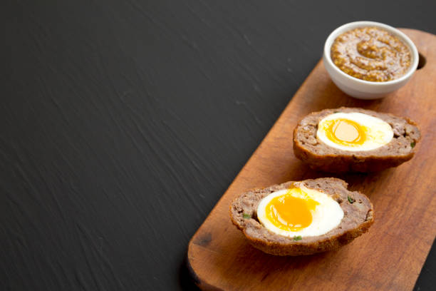 istock Homemade Scotch Eggs on a rustic wooden board on a black background, side view. Copy space. 1335175034
