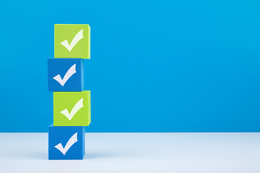 Checkmarks on four light green and blue  blocks on white table against blue background with copy space