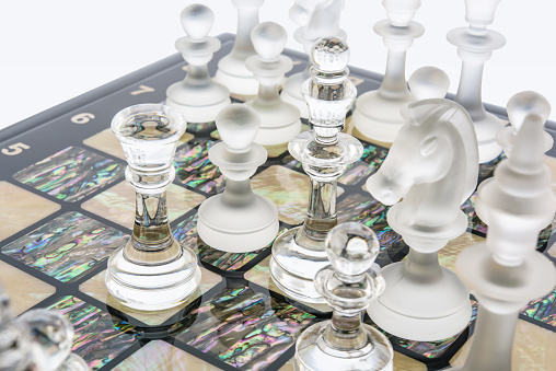 Transparent different glass chess pieces figures standing on pearl board in white. Glossy and matte set of shapes. game concept of confrontation.