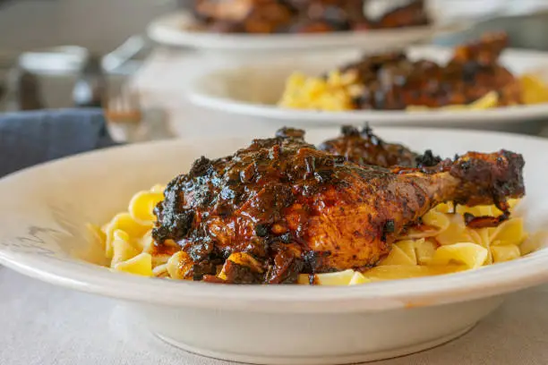 Italian braised chicken dish with pasta and delicious red wine sauce or gravy. Served on a white deep pasta plate on a table. Closeup and front view with blurred background