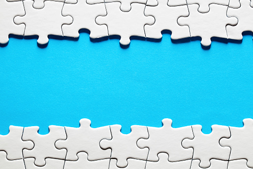 Empty blue background surrounded by white jigsaw puzzle pieces with copy space.