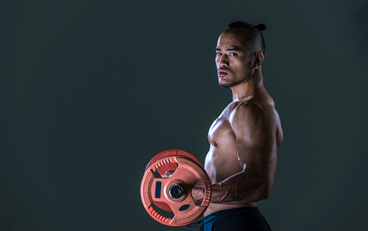 Muscular man working out in gym doing exercises with barbell, weights at biceps, looking at camera.