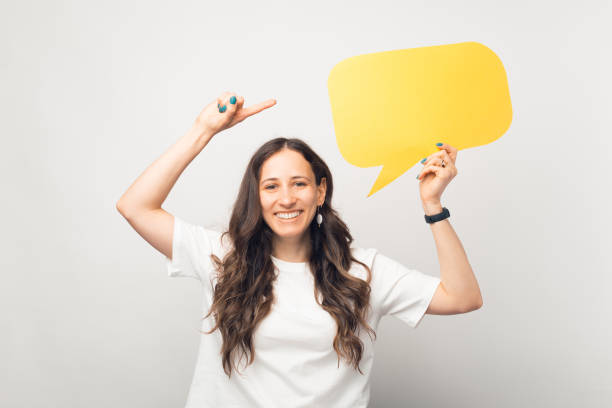 istock Smiling pretty woman is holding a yellow bubble speech and points at it. 1335187912
