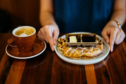 Image of an Asian woman eating waffle and having coffee break in cafe