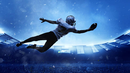 High jump. Professional American football player in motion, action during match at stadium. Sportsman in uniform catching ball. Concept of movement and action, sport lifestyle, competition