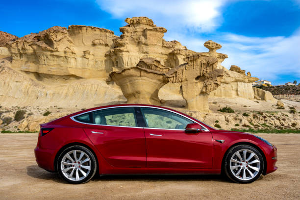 side view of a red Tesla Model 3 electric car with rock formation on the mediterranean coast and blue sky in Bolnuevo, Murcia, Spain. Side view of a red Tesla Model 3 electric car with rock formation on the mediterranean coast and blue sky in Bolnuevo, Murcia, Spain. tesla model 3 stock pictures, royalty-free photos & images