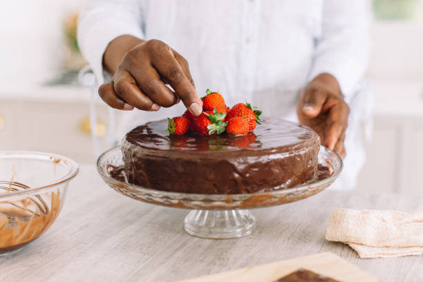 крупный план женщины, украшающей торт клубникой - dessert sweet food brown chocolate стоковые фото и изображения