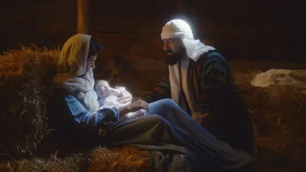Joseph talking with Mother Mary caressing baby Jesus on Christmas day in dark stable in Bethlehem