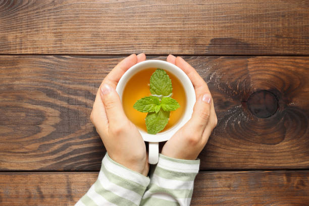 Woman hands hold cup of tea with mint leave top view Woman hands hold cup of tea with mint leave top view at the brown wooden table background mint tea stock pictures, royalty-free photos & images