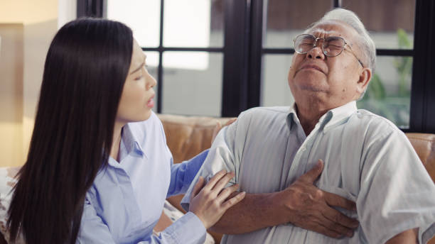 Woman supporting old father suffering with chest pain at home stock photo