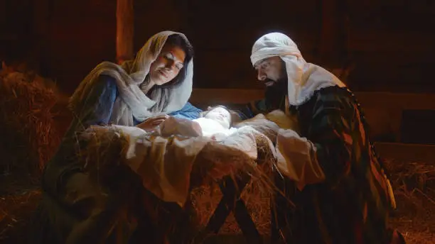 Photo of Mary and Joseph caressing baby Jesus in illuminated manger