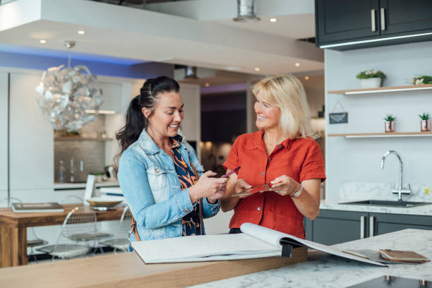 Helping A Customer A front view shot of a female saleswoman talking to a customer and discussing options for her kitchen and bathroom they are looking through a catalog of samples and she is using her mobile phone to show the assistant what they are working with. They are in a salesroom in Hexham in the North-East of England. showroom stock pictures, royalty-free photos & images