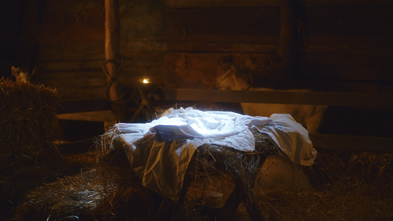 White sheet placed in illuminated manger prepared for baby Jesus Christ in dark inn barn in Bethlehem