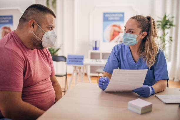 Man came to to receive a vaccine Two people, man sitting at vaccination center, female nurse is filling his medical record form. herd immunity photos stock pictures, royalty-free photos & images