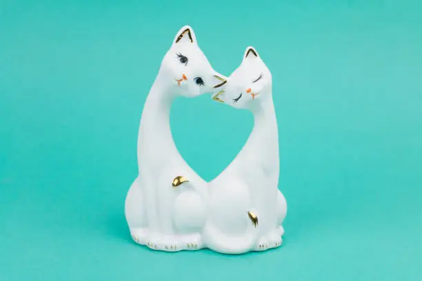 Photo of Porcelain figurine of two white cats. On a turquoise background