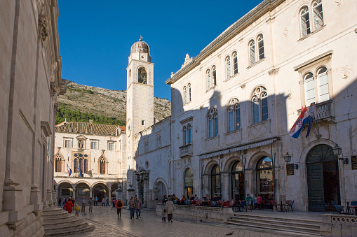 Pred Dvorom, Dubrovnik, Croatia, 16th October, 2019: St. Blaise's Church on the left and Sponza Palace and Clocktower at the end of the street in Luža Square