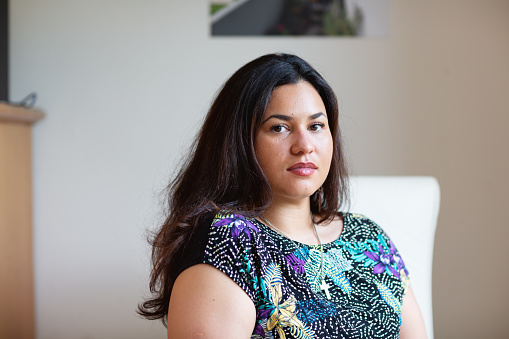 Portrait of a young hispanic woman with long black hair, wearing a dark shirt with coloful pattern and a jewelry pendant in form of a cross