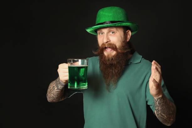 homem barbudo com cerveja verde no fundo preto. celebração do dia de são patrício - beer glass mustache beer color image - fotografias e filmes do acervo