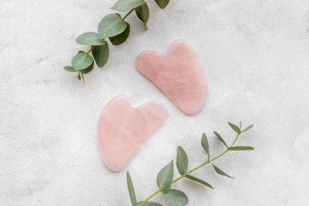 Rose quartz gua sha massage stone with green leaves stock photo