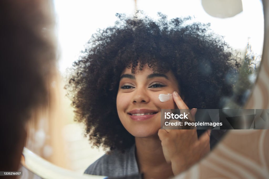 Shot of an attractive young woman applying moisturiser to her face at home A face that wakes the muscle in your chest Moisturizer Stock Photo