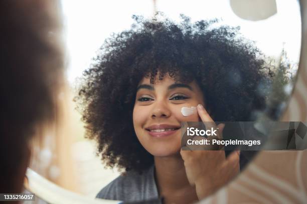 Shot Of An Attractive Young Woman Applying Moisturiser To Her Face At Home Stock Photo - Download Image Now