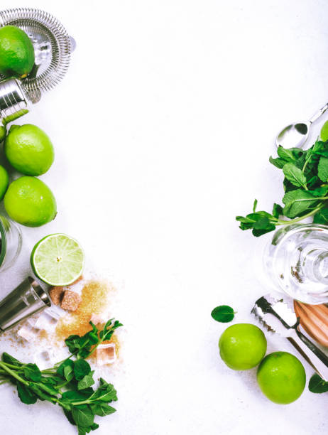 istock Mojito cocktail making. Mint, lime, ice, white rum, cane sugar - ingredients and bar utensils. Top view, white background. Flat lay 1335229154