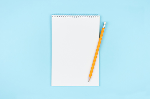 Blank open notepad with yellow pencil on blue background.