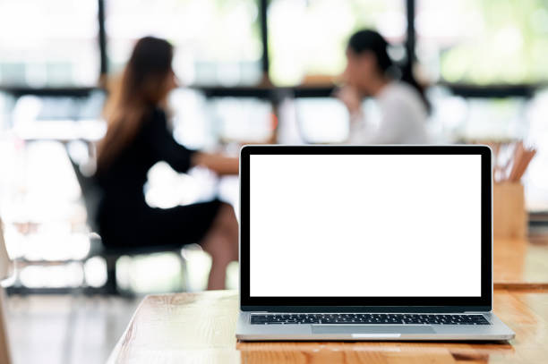 istock Mockup blank screen laptop computer on wooden table with blurred business people background. 1335233539