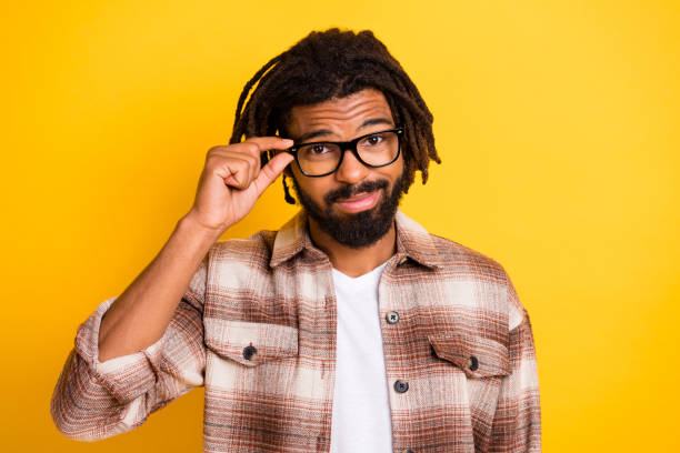 retrato fotográfico de un hombre brunet tocando gafas sin dudar de haber usado ropa casual aislada sobre un fondo de color amarillo vivo - reflection dreadlocks men businessman fotografías e imágenes de stock